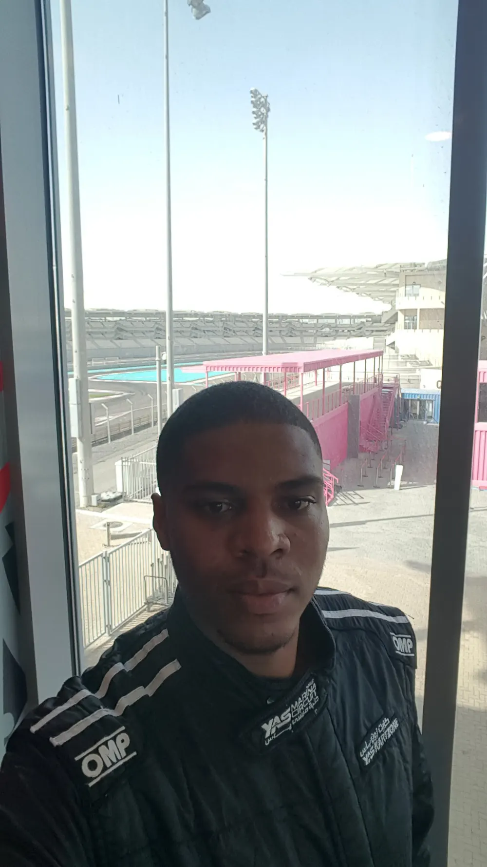 Neil in a black racing suit beside a window overlooking Yas Marina Circuit